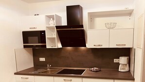 Una cocina compacta con armarios blancos, un microondas negro, una cafetera y un lavamanos.