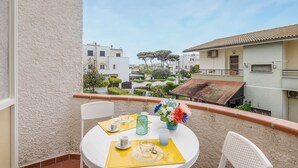 Ein Balkon mit einem Tisch für zwei Personen, mit Blick auf ein Wohngebiet mit weißen Gebäuden und einem Baum.