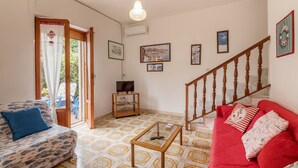 Ein Wohnzimmer mit einem roten Sofa, einem blau gemusterten Sofa, einem Glastisch und einer Treppe.
