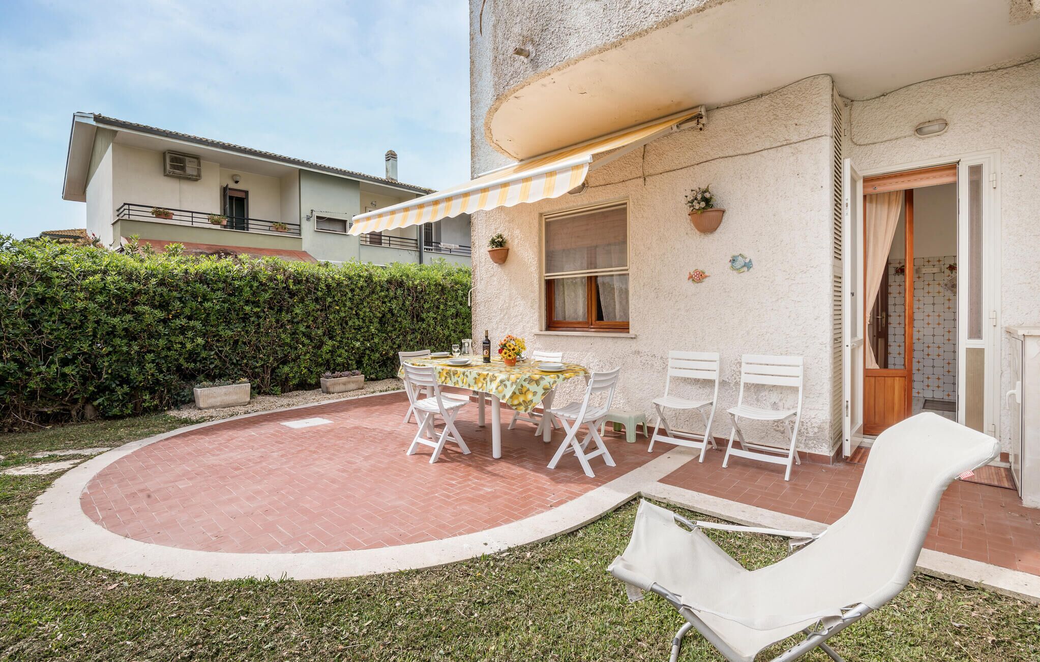 Un patio con mesa lista para comer, rodeado de sillas blancas y una sillón reclinable blanco.