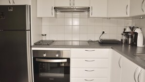 Ett kök med ett kylskåp i rostfritt stål, en inbyggd ugn, vita skåp och en bänkskiva med olika köksapparater.
