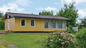Ett gult, enplanshus med ett stort fönster, en dörr och en liten veranda.