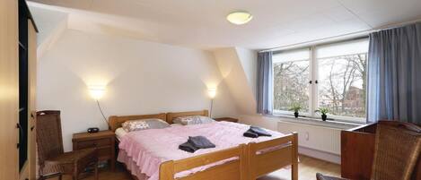Une chambre à coucher avec un lit en bois, deux tables de chevet, une chaise, un bureau et une fenêtre avec des rideaux.