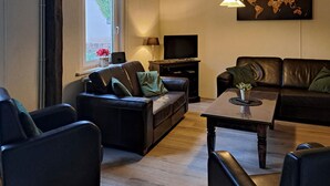 Ein modernes Wohnzimmer mit Ledersofas, einem Flachbildfernseher und einer Weltkarte als Wandkunst.