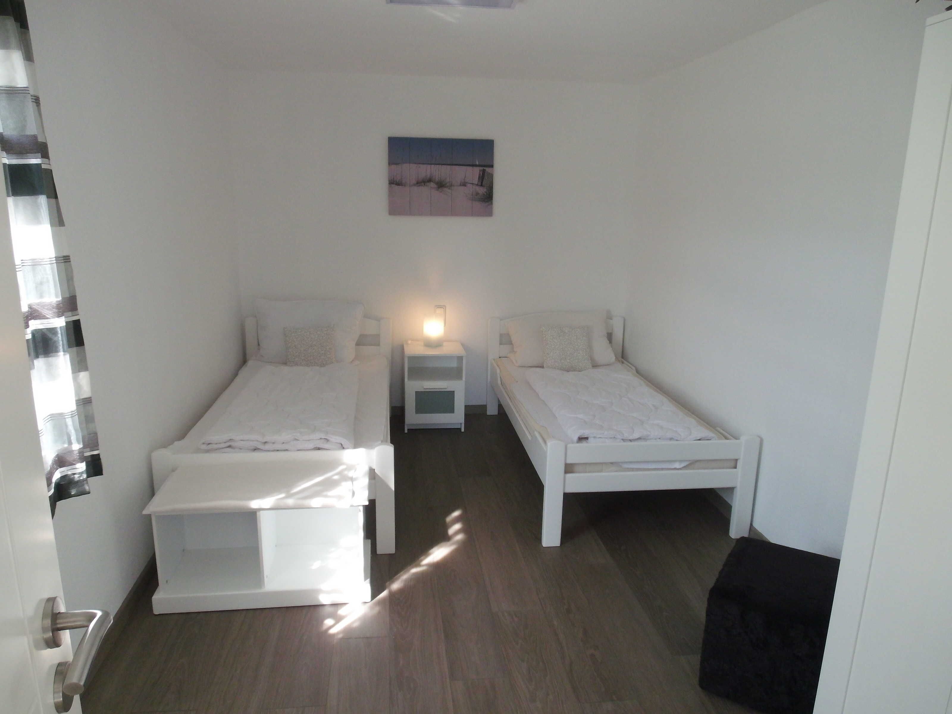 Ein Schlafzimmer mit zwei Einzelbetten, einem Nachttisch mit Lampe, einem kleinen Bild an der Wand und einer Tür mit Vorhang.