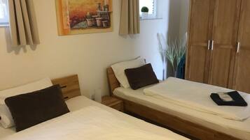 A room with two beds, a wooden wardrobe, a window with curtains, and a painting on the wall.