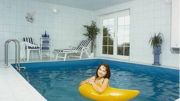 A swimming pool with a person on a yellow float, white tiled walls, and a window.