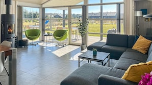 A modern living room with a fireplace, green chairs, a sofa, and a view of a garden and buildings. - Gorgeous home in Ejstrupholm with sauna (Ejstrupholm)