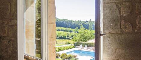 A view from a window overlooking a swimming pool with a landscaped garden and a hilly landscape in the distance.