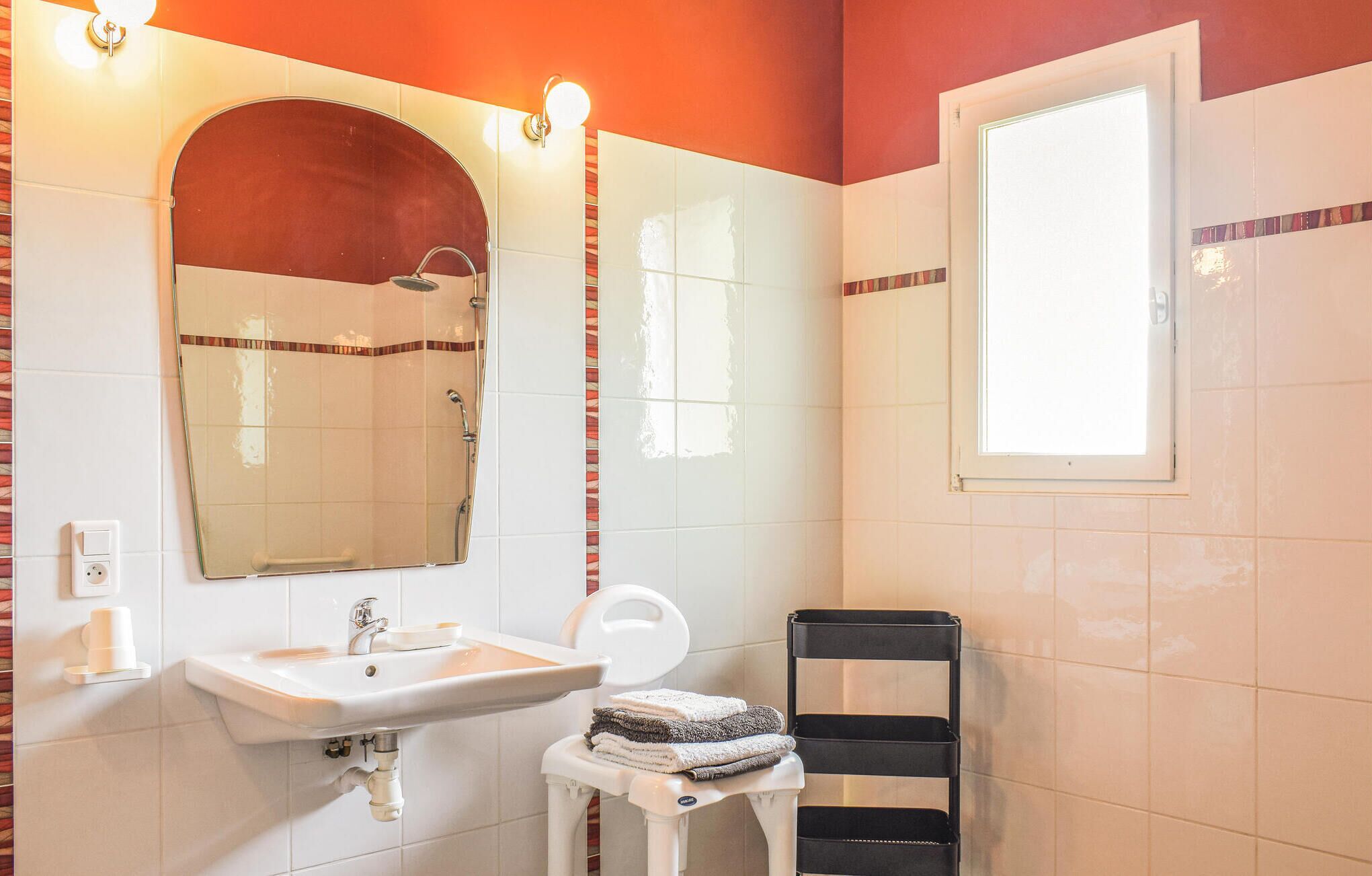 A bathroom with a sink, mirror, shower, and a window.