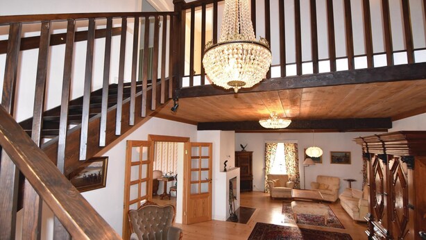 Un vaste espace de vie agrémenté d’un escalier en bois, d’un lustre et d’une grande fenêtre avec des rideaux.