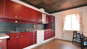 Une cuisine avec des meubles de rangement rouges, un lave-vaisselle, une cuisinière et une fenêtre avec des rideaux.