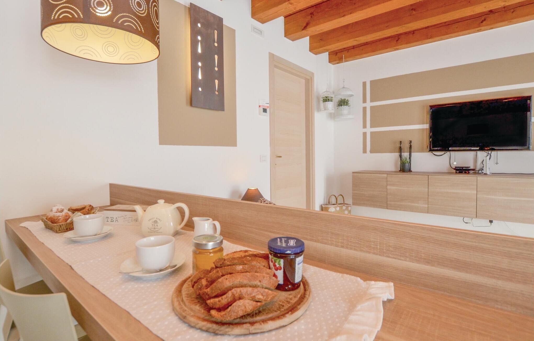 Colazione servita con pane, tè e marmellata su un tavolo in una stanza con travi in legno, televisione e mobiletto.