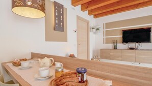 Ein Frühstückstisch mit Brot, Tee und Marmelade in einem Raum mit Holzbalken, einem Fernseher und einem Schrank.