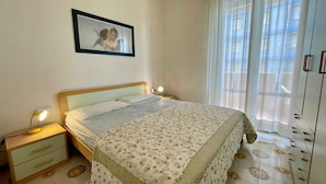 Ein Schlafzimmer mit einem Bett, Nachttischlampen, einem gerahmten Bild, einem Fenster mit Vorhängen und einem Fliesenboden.
