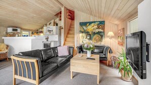 Una sala de estar acogedora con un sofá de cuero negro, una mesa de centro de madera, un televisor y una zona de cocina con microondas y refrigerador.