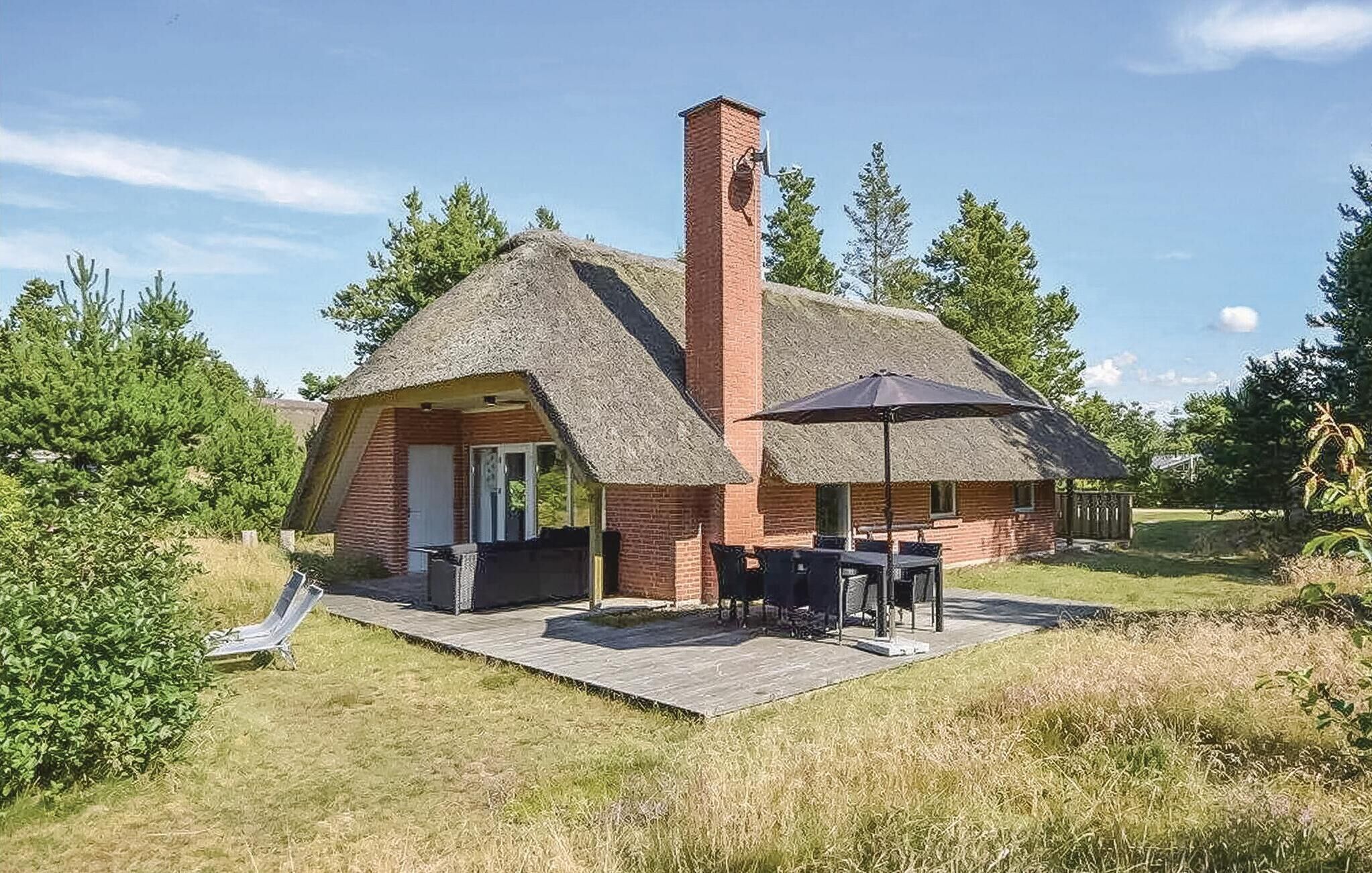 A thatched-roof cottage with a brick chimney, a patio with a table and chairs, and a wooden deck.