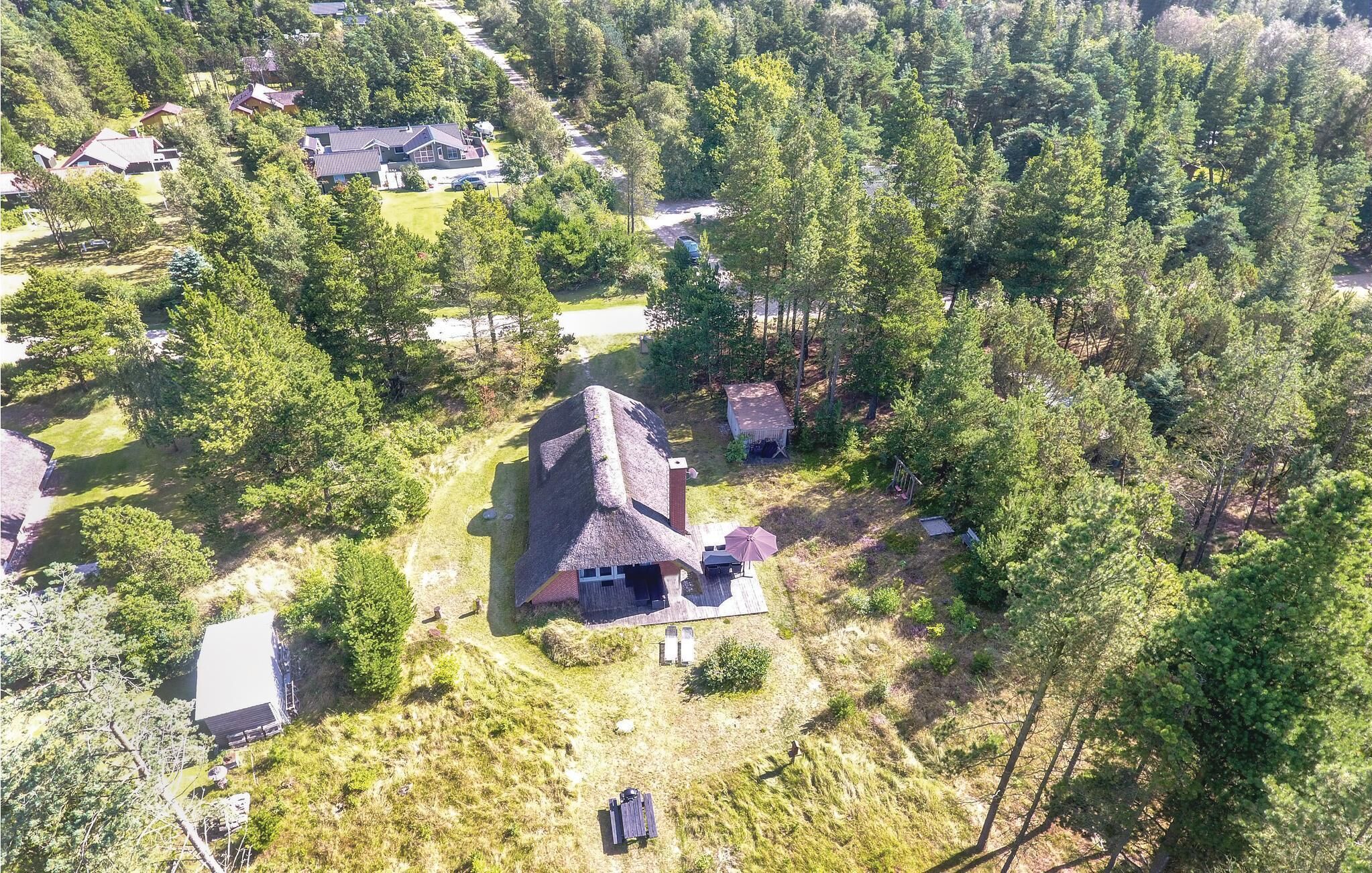 An aerial view of a secluded house surrounded by dense forest, with a thatched roof and a small patio area.