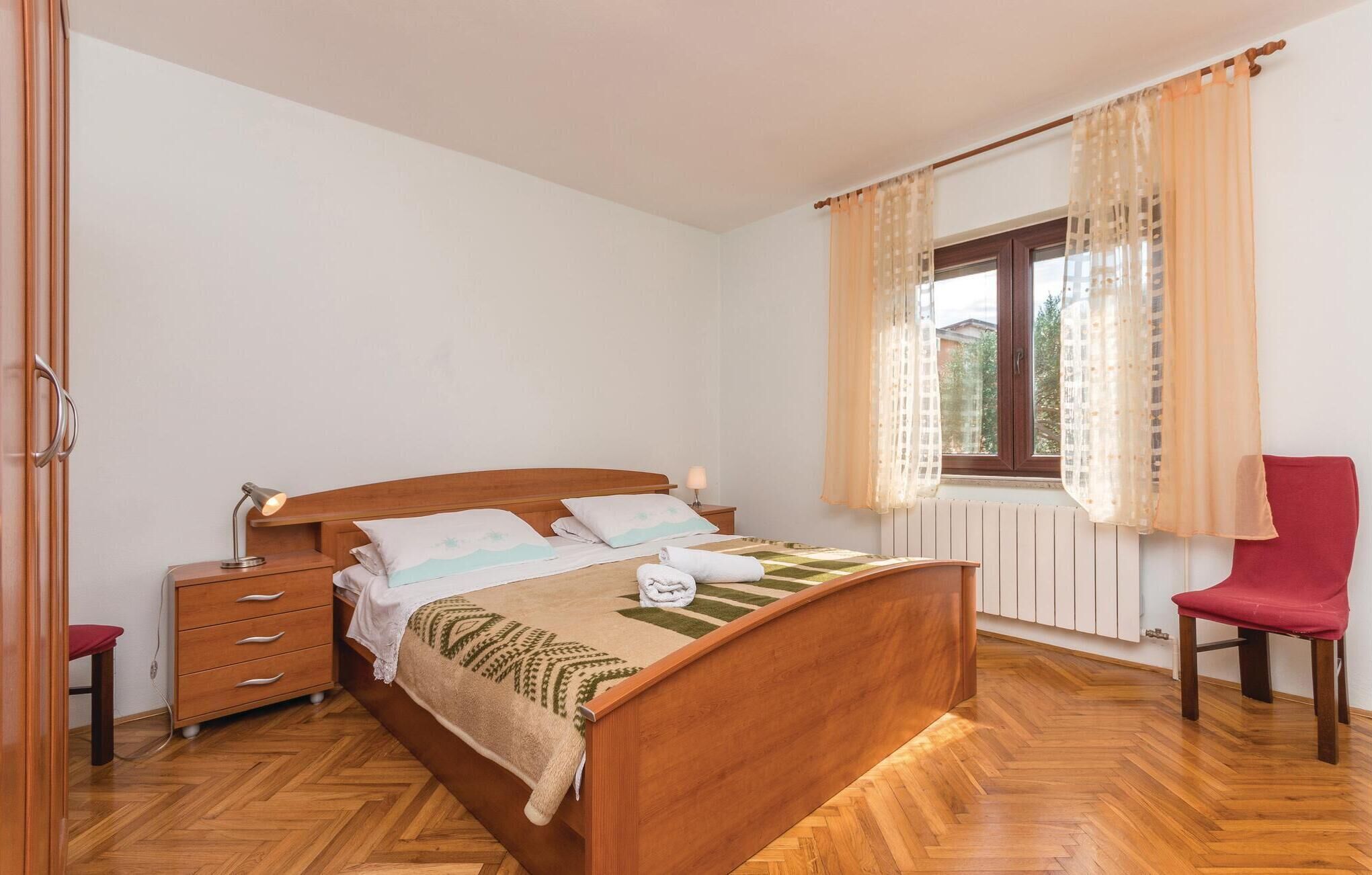 A bedroom with a wooden bed, bedside tables, a chair, and a window with curtains.