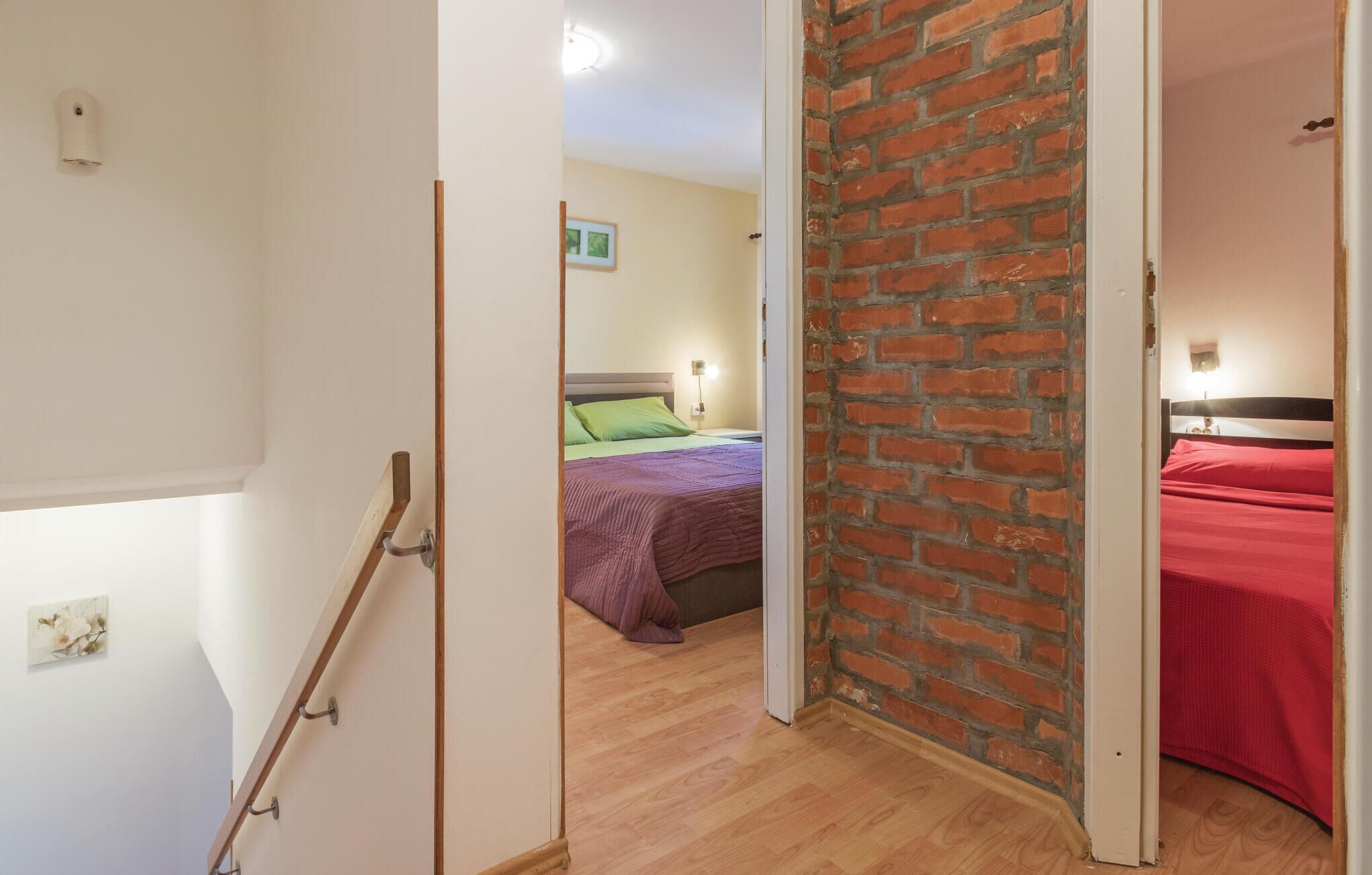 A narrow hallway leading to a bedroom with a brick wall and a wooden floor.