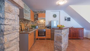 Une cuisine compacte aux murs en pierre, dotée d’un four encastré et d’un petit réfrigérateur.