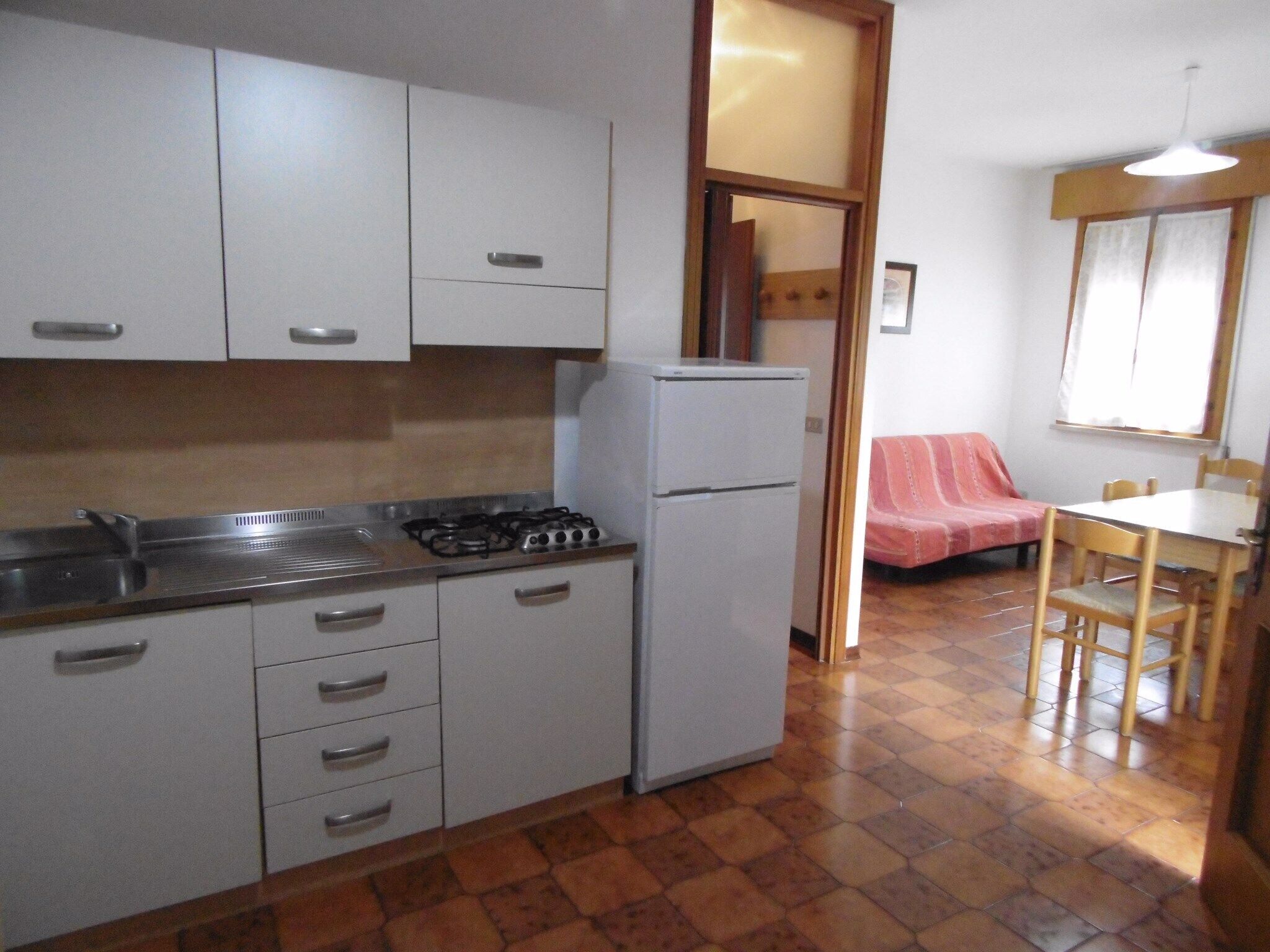 A compact kitchen with white cabinets, a gas stove, and a white refrigerator. There is a dining area with a table and chairs, and a red blanket on a chair.
