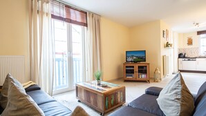 Una sala de estar con un sofá, una mesa de centro y un televisor. Hay una puerta corrediza de vidrio que da a un balcón.