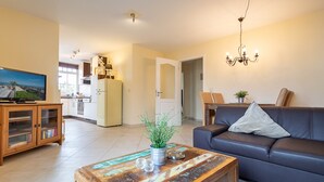 Una sala de estar con televisión, sofá, mesa de centro y una cocina al fondo.
