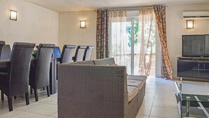 A dining area with a table and chairs, a wicker sofa, a television, and an air conditioning unit. - Stunning home in Moriani Plage (Moriani Plage)