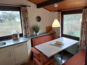 A cozy kitchen with a wooden bench, a table, a clock, and a window with curtains.