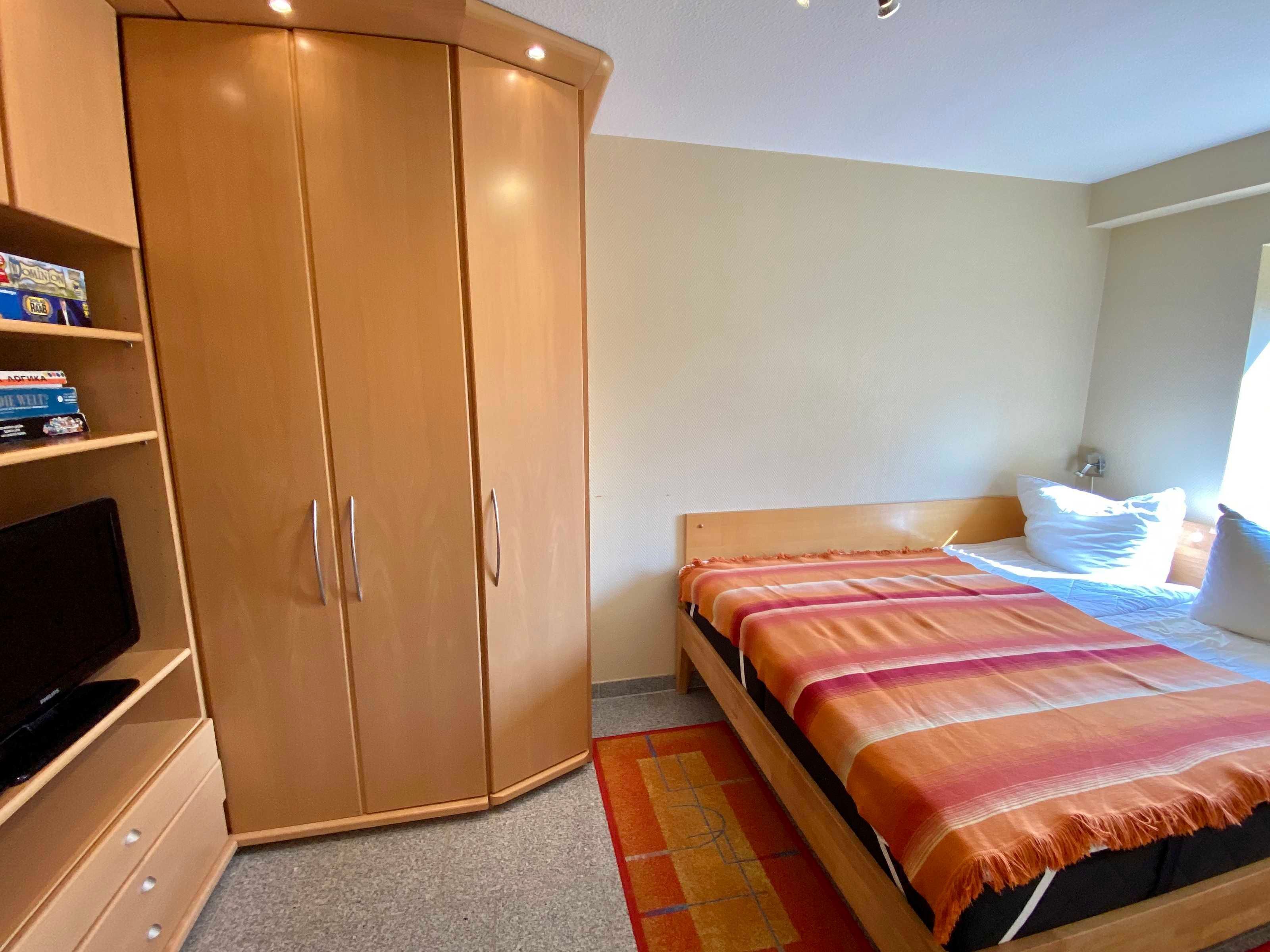A bedroom with a bed, a wardrobe, a television, and a window.