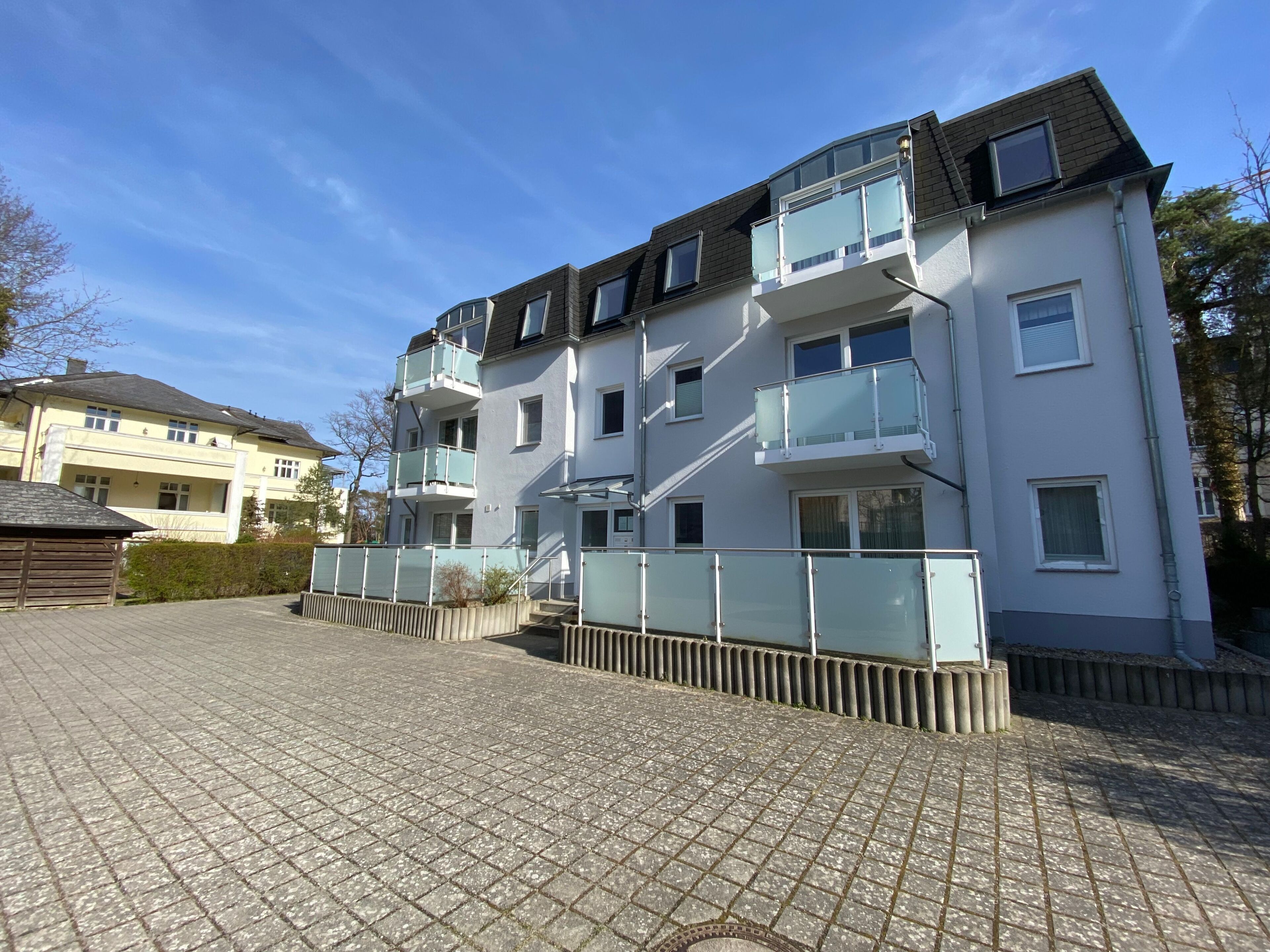 Edifício residencial com várias andares, varandas, entrada pavimentada e céu claro.