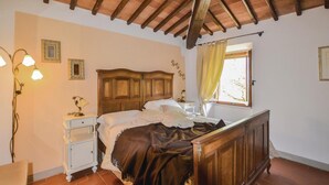 A bedroom with a wooden bed, a nightstand, a lamp, and a window with curtains.