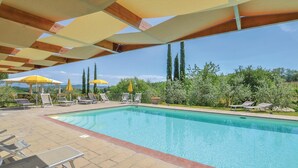 A swimming pool with lounge chairs and umbrellas, surrounded by greenery and tall trees.