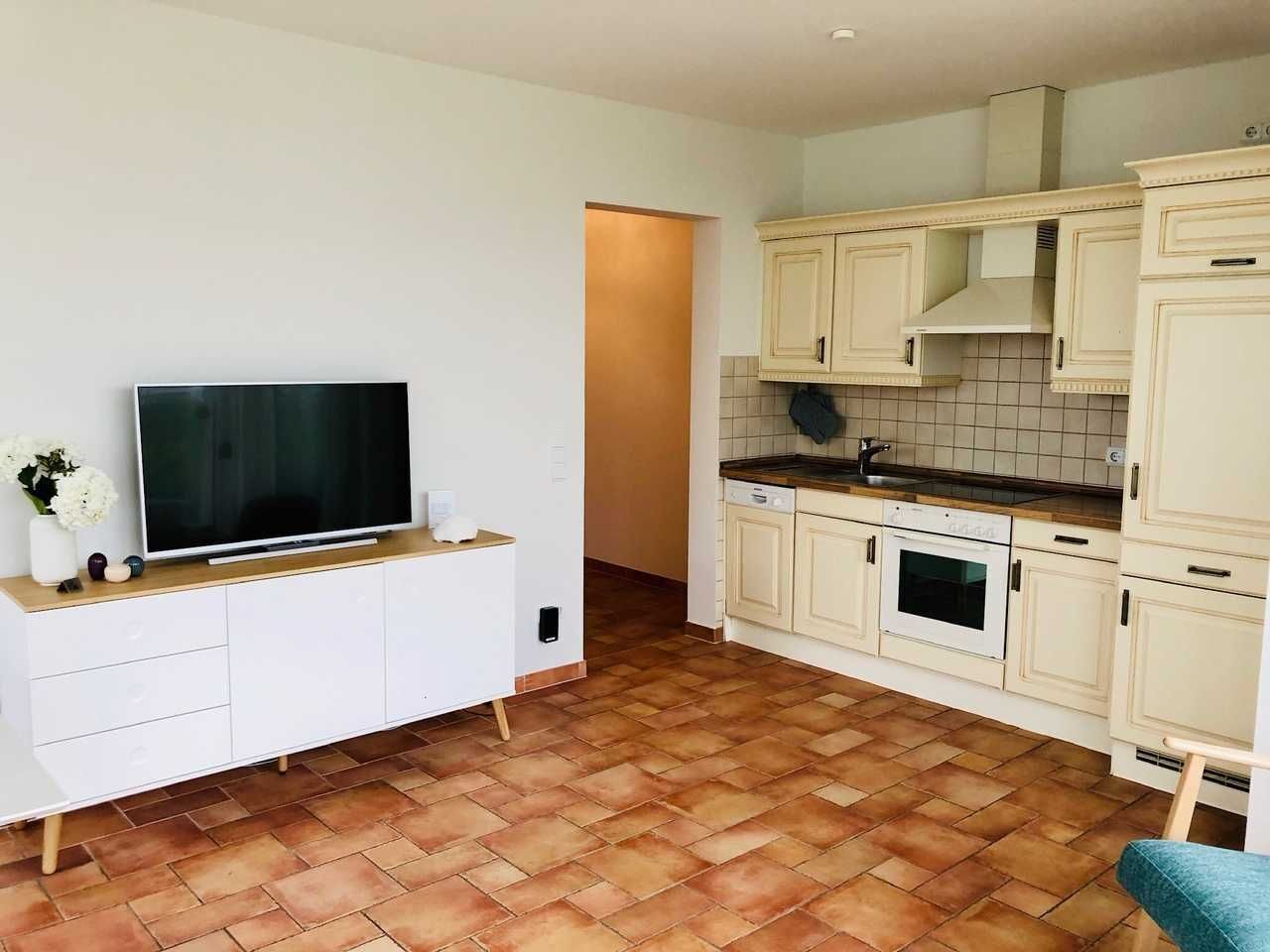 Eine kompakte Küche mit weißen Schränken, einem eingebauten Backofen und einem Fernseher auf einer Holzkonsolle.