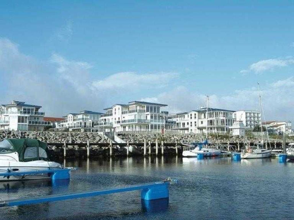 Un puerto deportivo con barcos amarrados, un edificio frente al agua y un cielo despejado.