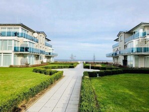Un hôtel moderne avec un chemin central menant à l’entrée, entouré de pelouses bien entretenues et offrant une vue dégagée sur la mer.