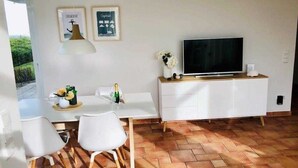 Moderni olohuone, jossa on litteänäyttöinen televisio, valkoiset huonekalut ja laatoitettu lattia.
