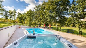 En swimmingpool med jacuzzi, omgivet af træer og solstole.