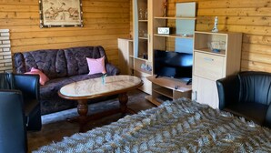 Ein gemütliches Zimmer mit Holzbalkendecke, einer Couch, einem Couchtisch, einem Fernseher und einem Bücherregal.