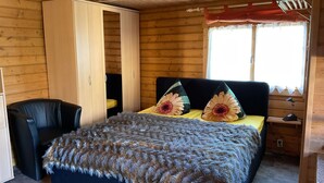 Ein Schlafzimmer mit Bett, Schrank, Stuhl, einem Fenster mit Vorhängen und einem Nachttisch mit Lampe.