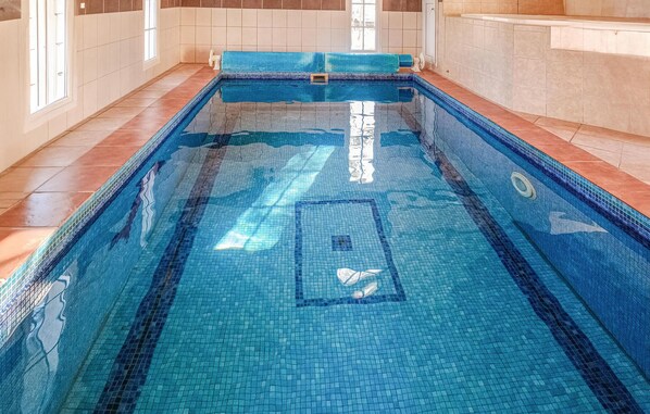 A rectangular indoor swimming pool with clear blue water, tiled walls, and a tiled floor.