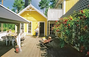 A wooden deck with outdoor furniture, a covered seating area, and a garden with red flowers.