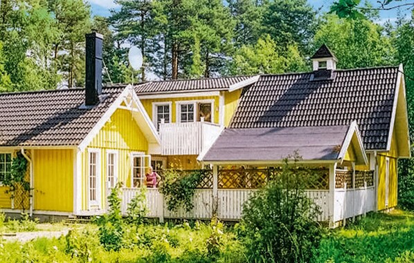 A yellow house with a grey roof, white porch, and a small tower-like structure on the roof.