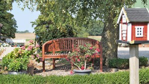A wooden bench surrounded by potted plants and a birdhouse. - Lachmöwe, apartment 3 pers. - Vacation farm Kai Hansen (Neustadt in Holstein)
