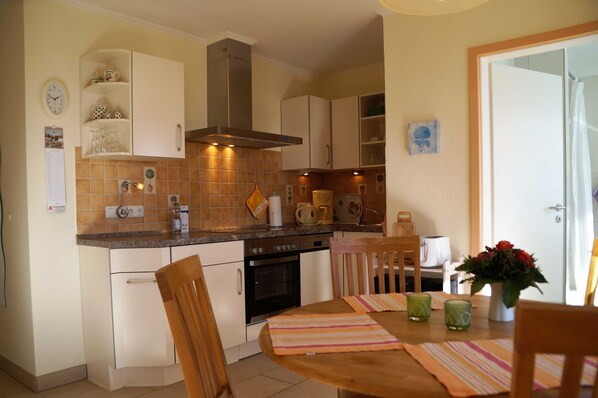 A compact kitchen with white cabinets, a stove, and a dining area with a table and chairs. - Lachmöwe, apartment 3 pers. - Vacation farm Kai Hansen (Neustadt in Holstein)