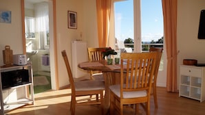 A dining area with a wooden table, chairs, and a view through the window. - Lachmöwe, apartment 3 pers. - Vacation farm Kai Hansen (Neustadt in Holstein)