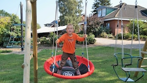 A child on a swing set in a park with a house in the background. - Lachmöwe, apartment 3 pers. - Vacation farm Kai Hansen (Neustadt in Holstein)