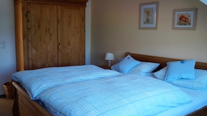 A double bed with blue bedding, a wooden wardrobe, and two framed floral pictures on the wall. - Lachmöwe, apartment 3 pers. - Vacation farm Kai Hansen (Neustadt in Holstein)