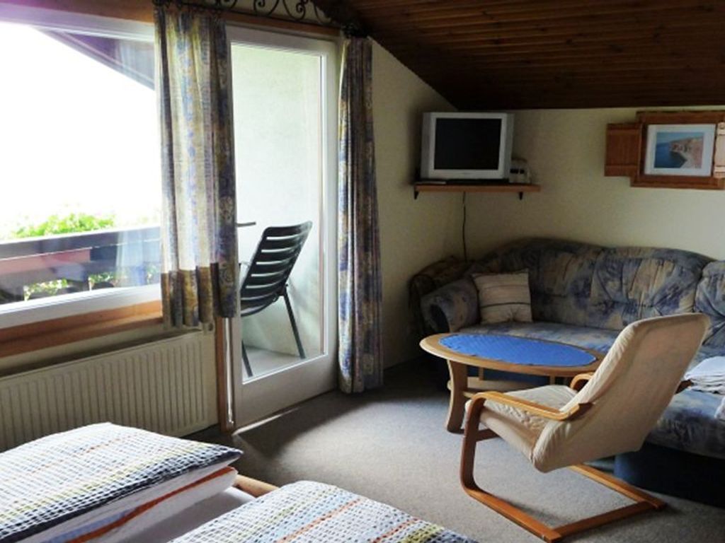 Une pièce comprenant un canapé, un fauteuil, une petite table, un téléviseur et une fenêtre avec des rideaux.